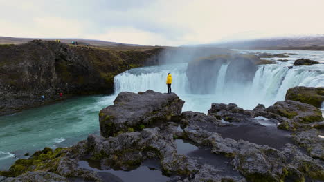 Aerial-View-Of-Man-Standing-On-The-Cliff-At-Godafoss-Waterfall-In-Iceland---Drone-Shot