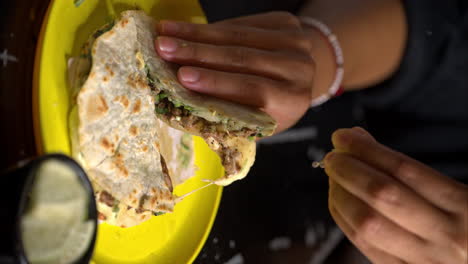 Vertical-slow-motion-of-a-woman's-pair-of-hands-holding-a-quesadilla-taco-on-a-yellow-plate-and-squeezing-some-lime-lemon-juice-on