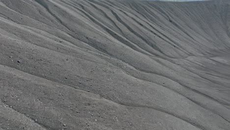 Black-volcanic-sand-surface-on-the-crater-rim,-close-up-aerial-view