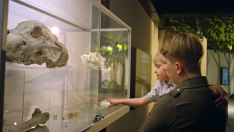 Little-girl-in-her-mother-arms-looking-at-animal-skeleton-in-a-museum,-side-view