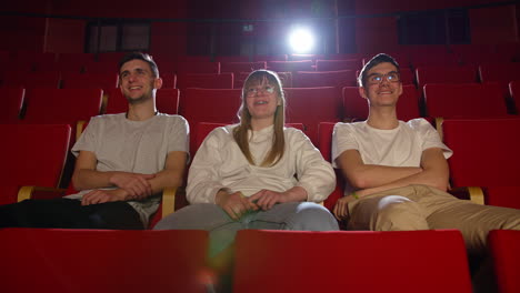 Three-friends-in-the-cinema-hall,-having-fun-watching-a-film,-front-view