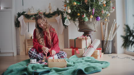 Glückliche-Frau,-Die-Zu-Hause-Ein-Band-An-Ein-Verpacktes-Weihnachtsgeschenk-Bindet