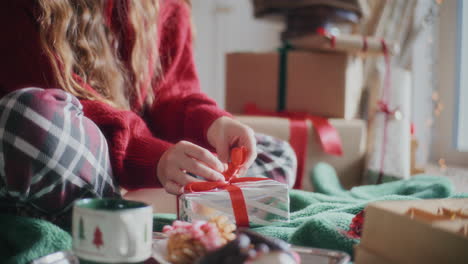 Woman-making-ribbon-bow-on-wrapped-Christmas-gift-at-home