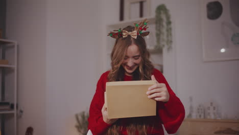 Woman-opening-gift-box-while-standing-at-home