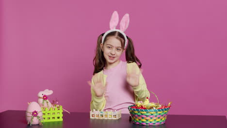 Joyful-child-putting-bunny-ears-on-her-head-and-waving-at-camera