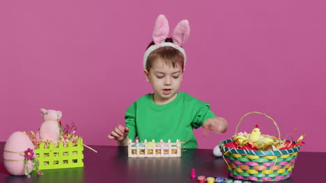 Happy-toddler-with-bunny-ears-arranging-basket-filled-with-painted-eggs