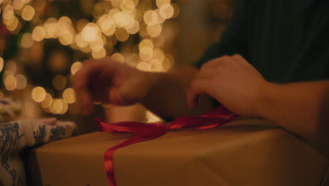 Man-tying-ribbon-to-Christmas-gift-box-at-home
