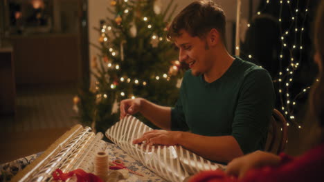 Young-man-wrapping-gift-sitting-by-female-friend