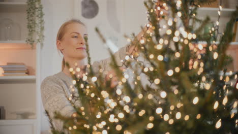 Frau-Schmückt-Den-Weihnachtsbaum-Mit-Leuchtenden-LED-Lichtern