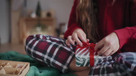 Woman-tying-ribbon-on-wrapped-Christmas-gift-at-home