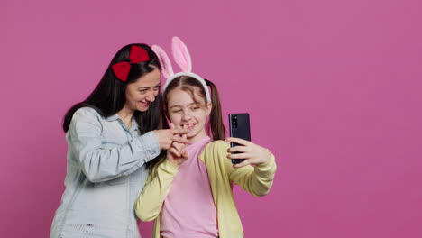 Playful-cheery-mother-and-girl-smiling-for-photos-on-smartphone