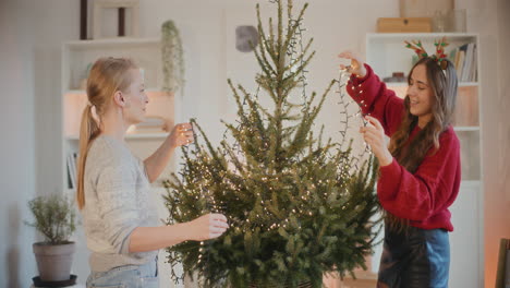 Freundinnen-Schmücken-Den-Weihnachtsbaum-Mit-Lichtern