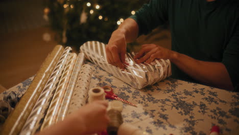 Man-wrapping-gift-paper-on-box-at-table