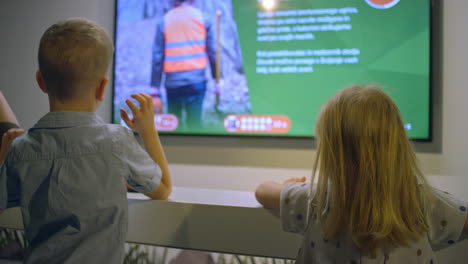 Two-little-children-looking-at-a-screen-in-a-natural-history-museum,-rear-view