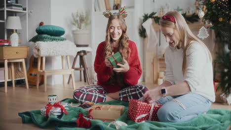 Playful-sisters-wrapping-Christmas-gifts-at-home
