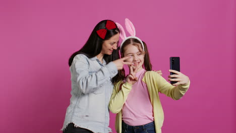 Playful-cheery-mother-and-girl-smiling-for-photos-on-smartphone