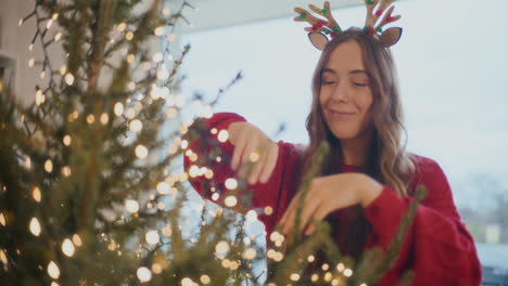 Young-woman-adjusting-led-lights-on-Christmas-tree