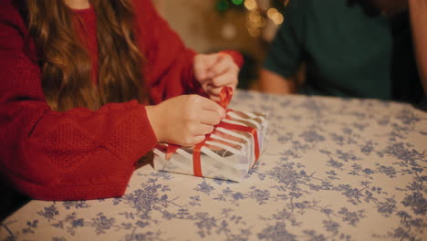 Woman-tying-ribbon-on-gift-box-sitting-by-friend