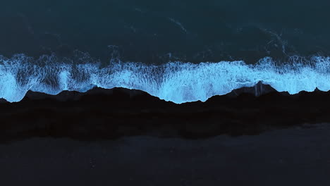 Dark-blue-ocean-waves-splashing-black-sand-beach,-aerial-top-down-shot