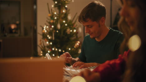 Man-wrapping-Christmas-present-sitting-by-female-friend