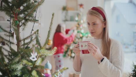 Beautiful-young-woman-drinking-coffee-near-Christmas-tree-at-home