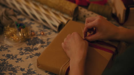 Woman-tying-ribbon-on-gift-box-at-table