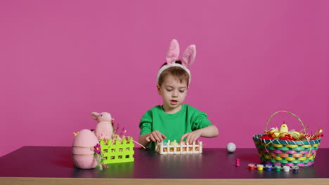 Happy-toddler-with-bunny-ears-arranging-basket-filled-with-painted-eggs
