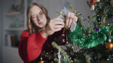 Cheerful-woman-hanging-bauble-on-Christmas-tree-at-home