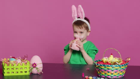 Entzückendes-Kleines-Kind,-Das-Am-Tisch-Mit-Einem-Ausgestopften-Kaninchen-Und-Einem-Rosa-Ei-Spielt