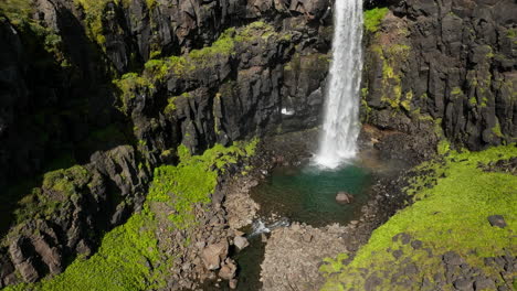 Waterfall-tumbling-down-over-the-tall-black-rocky-cliff,-aerial-shot