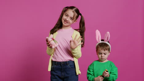Cute-brother-and-sister-posing-against-pink-background-in-studio