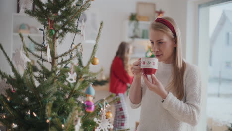 Beautiful-young-woman-smiling-while-drinking-coffee-near-Christmas-tree