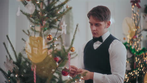 Young-man-in-tuxedo-decorating-Christmas-tree-at-home