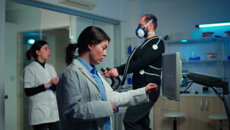 Doctor-sport-scientist-checking-EKG-scan-at-monitor-while-man-with-mask-running