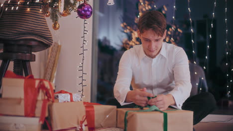 Man-tying-ribbon-on-wrapped-gift-box-at-home-during-Christmas