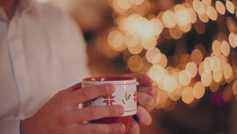 Hombre-Sosteniendo-Una-Taza-De-Café-En-Casa-Iluminada-Durante-La-Navidad