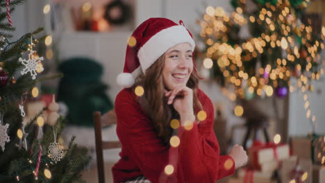 Cheerful-woman-in-Santa-hat-sitting-with-hand-on-chin-at-decorated-home