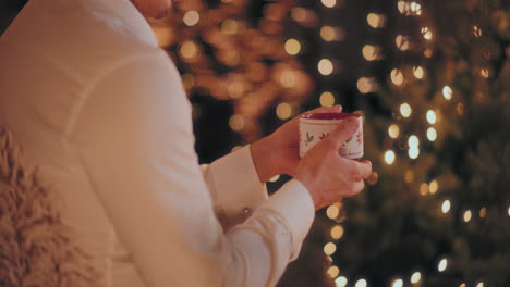 Mann-Hält-Kaffeetasse-In-Der-Hand,-Während-Er-Zu-Weihnachten-Im-Beleuchteten-Haus-Sitzt