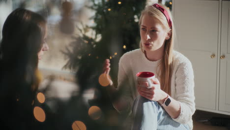 Beautiful-woman-with-coffee-cup-talking-to-sister-at-home-during-Christmas