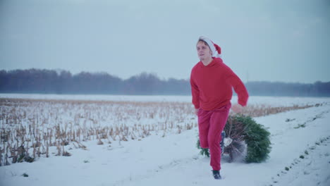 Man-pulling-Christmas-tree-while-running-on-snow-covered-landscape