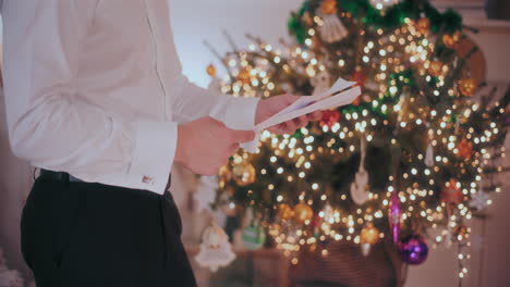 Man-opening-letter-with-decorated-Christmas-tree-in-background