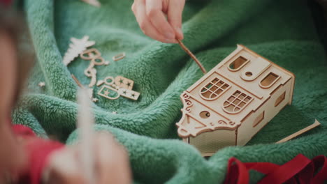 Cropped-woman-assembling-cardboard-house-ornament-on-floor-during-Christmas