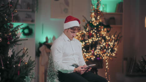 Mann-Benutzt-Digitales-Tablet,-Während-Er-Zu-Weihnachten-Auf-Einem-Stuhl-In-Einem-Beleuchteten-Zuhause-Sitzt