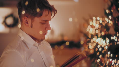 Handsome-man-reading-book-in-illuminated-home-during-Christmas