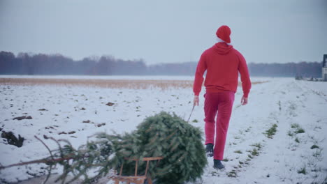 Hombre-Tirando-Del-árbol-De-Navidad-En-El-Paisaje-Cubierto-De-Nieve.