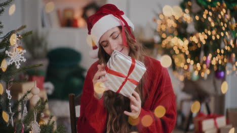 Glückliche-Frau-Mit-Weihnachtsmütze-Hält-Geschenkbox-Im-Dekorierten-Zuhause