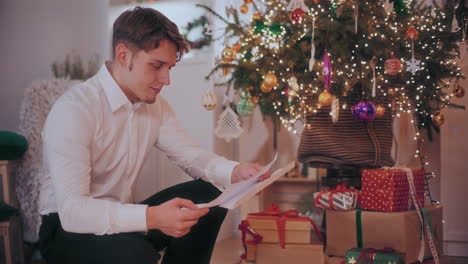 Glücklicher-Mann-Liest-Brief-Mit-Weihnachtsgeschenken-Und-Geschmücktem-Baum