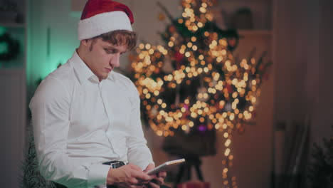 Hombre-Usando-Una-Tableta-Digital-Mientras-Está-Sentado-En-Una-Casa-Iluminada-Durante-La-Navidad
