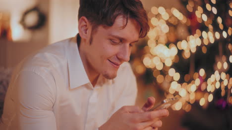 Glücklicher-Mann,-Der-Zu-Weihnachten-Sein-Smartphone-Im-Beleuchteten-Zuhause-Benutzt