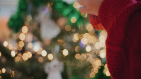 Weibliche-Hände-Schmücken-Beleuchteten-Weihnachtsbaum-Mit-Christbaumkugel-Zu-Hause